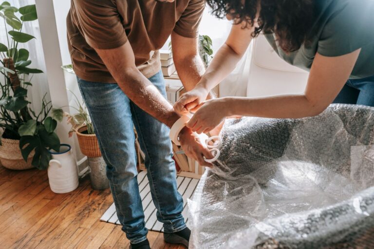 Dos personas envolviendo un sillón con plástico de burbujas antes de la mudanza